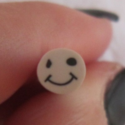 Conta redonda creme com rosto sorridente preto segurada entre dedos com unhas pintadas