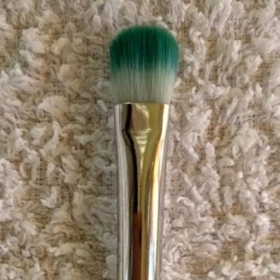 Pincel de maquilhagem verde com cabo metálico prateado em tecido creme