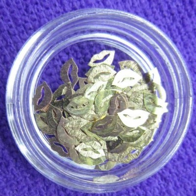 Pote de vidro com lantejoulas douradas em forma de lábios sobre tecido roxo