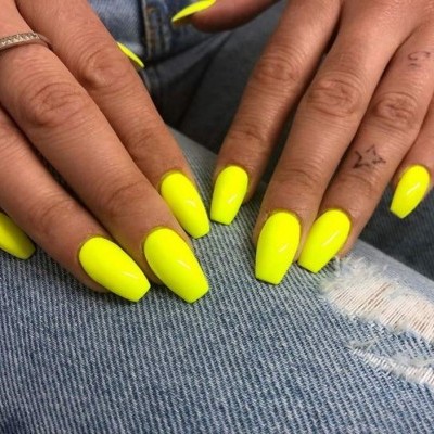 Unhas artificiais amarelo néon sobre jeans azul rasgado
