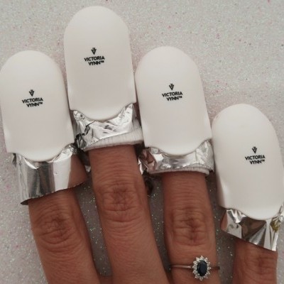 Protetores de unhas brancos com texto VICTORIA VYNN nos dedos.