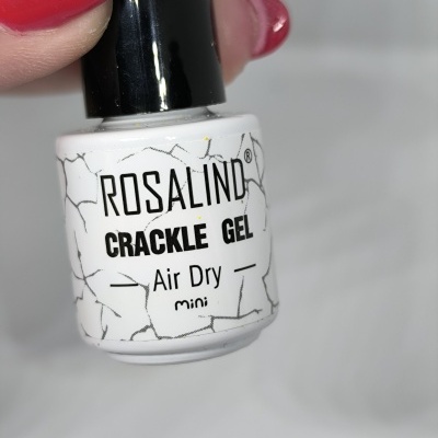 Frasco branco de verniz gel para unhas da marca Rosalind com tampa preta, segurado por mão com unhas vermelhas