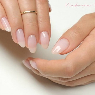 Mãos femininas com unhas manicuras naturais e frasco de verniz gel base da marca Victoria Vynn