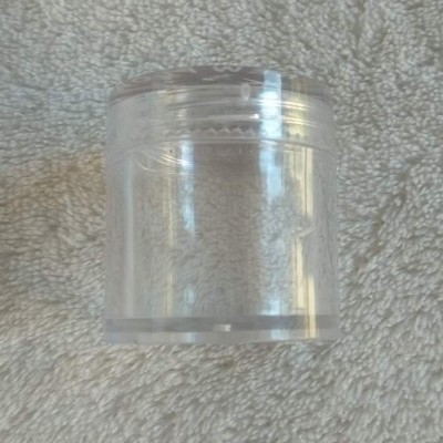 Frasco plástico transparente cilíndrico com tampa sobre tecido cinzento