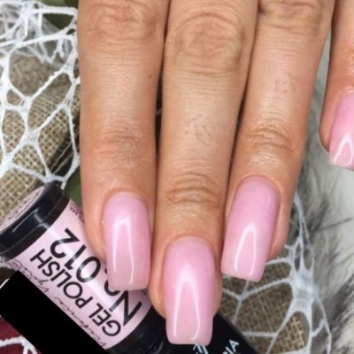 Mão feminina com unhas rosa brilhantes segurando frasco de verniz gel preto e rosa sobre renda branca.