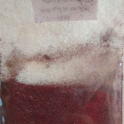 Pacote transparente com pó vermelho escuro com brilho e etiqueta branca