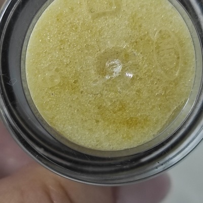 Parte inferior de frasco com produto amarelo granuloso e tampa preta