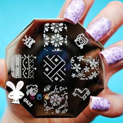 Placa octagonal prateada para carimbos de unhas com designs florais e geométricos brancos, segurada por mão com unhas lilás florais.