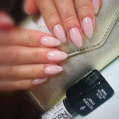 Unhas com verniz gel rosa claro e frasco de verniz gel preto em superfície dourada