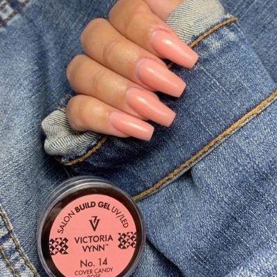 Frasco de gel para unhas Victoria Vynn No. 14 sobre tecido jeans com unhas pintadas rosa nude.