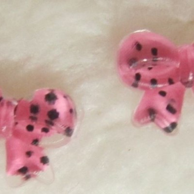 Dois laços cor-de-rosa com manchas pretas em plástico, sobre superfície clara