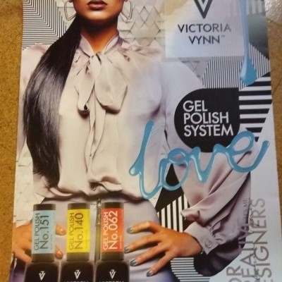 Mulher com camisa bege e calças azul claras segurando produtos de gel polish VICTORIA VYNN.