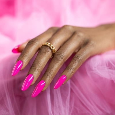 Mão feminina com unhas fúcsias e anel dourado sobre tecido rosa