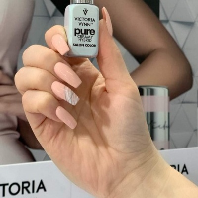 Frasco de verniz de unhas Victoria Vynn segurado por mão com unhas nude e padrão branco