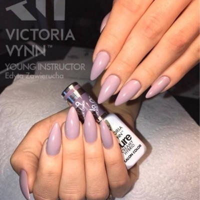 Unhas longas lilás claro brilhantes segurando frasco de verniz Victoria Vynn em fundo escuro