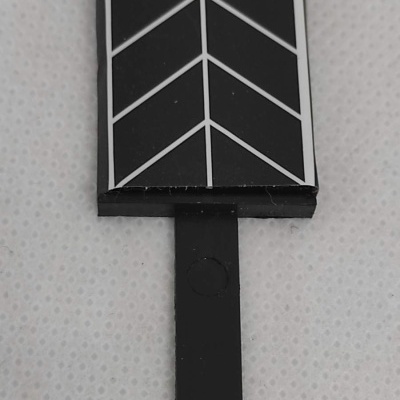 Peça plástica preta com padrão branco em espinha de peixe sobre superfície branca pontilhada