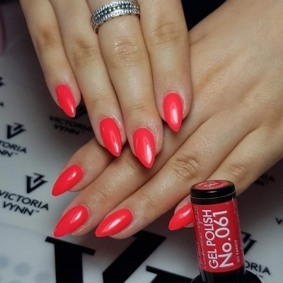 Mãos com unhas almendradas pintadas de cor salmão forte e brilhante, frasco de verniz gel 'No. 901' da marca Victoria Vynn em cima de mesa branca com logotipos pretos.