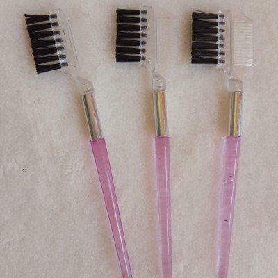 Três escovas de maquilhagem com cabo rosa e cerdas pretas sobre tecido branco