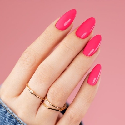 Mão feminina com unhas pintadas de rosa vibrante e anéis dourados