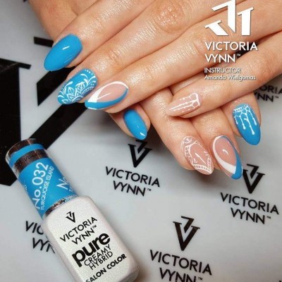 Mãos com unhas pintadas em azul e nude com designs brancos na superfície, frasco de verniz azul e outra embalagem branca da marca Victoria Vynn sobre fundo branco com logotipos.