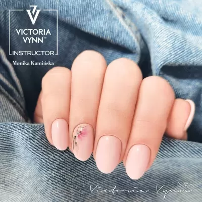 Unhas com verniz rosa claro e desenhos florais sobre tecido de ganga azul.