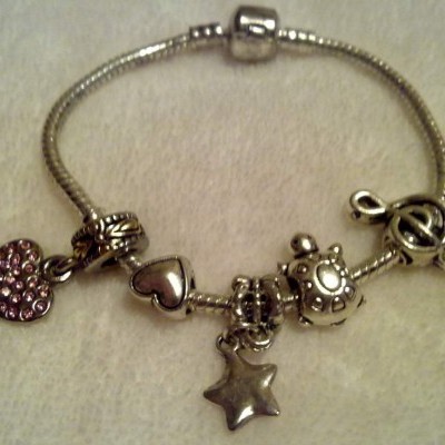 Pulseira prateada com quatro pendentes em fundo de tecido bege.