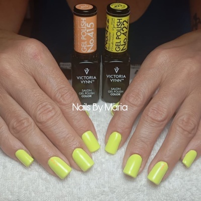 Mãos femininas com unhas amarelas quadradas e frascos de verniz gel Victoria Vynn laranja e amarelo