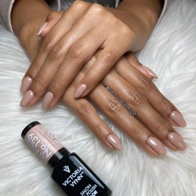 Mãos com unhas pintadas de rosa claro ao lado de um frasco de verniz gel preto em superfície felpuda branca.