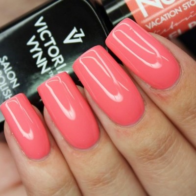 Verniz de unhas coral rosa brilhante em dedos com frascos de verniz