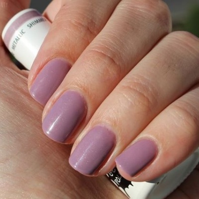 Mão com unhas pintadas de esmalte rosa lavanda fosco segurando frasco branco de esmalte