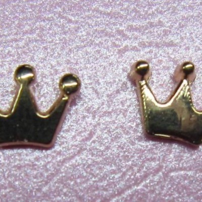 Par de brincos metálicos dourados em forma de coroa sobre fundo rosa texturizado