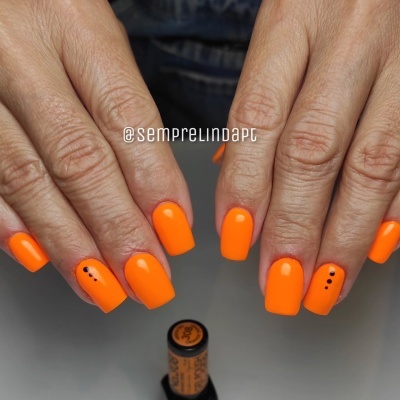 Mãos com unhas quadradas pintadas de verniz laranja fluorescente com pontos pretos