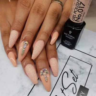 Unhas alongadas com gel polish cor pêssego e strass ao lado de verniz preto Victoria Vynn