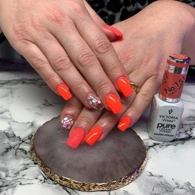 Mãos com unhas pintadas de laranja fluorescente com decoração de brilho e verniz fosco, garrafa de verniz VICTORIA VYNN.
