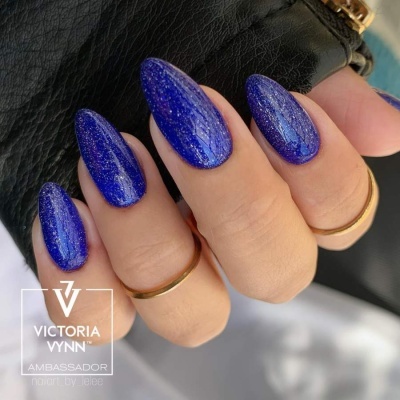 Unhas azuis brilhantes e cintilantes com anéis dourados segurando carteira preta