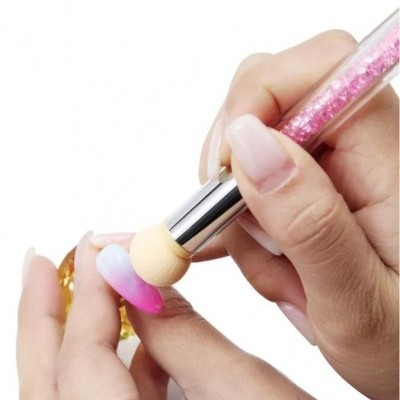 Pincel aplicador com partículas cor-de-rosa e esponja aplicadora em uso em unha artificial