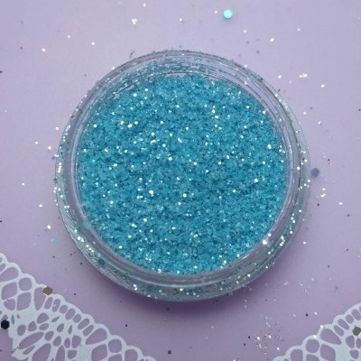 Pote de glitter azul cintilante em superfície lilás com detalhes brancos