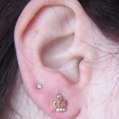 Orelha com dois brincos, um de pedra pequena e outro de coroa dourada com pedras.