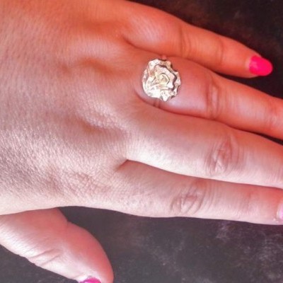 Anel prateado texturizado numa mão com unhas rosa sobre fundo escuro