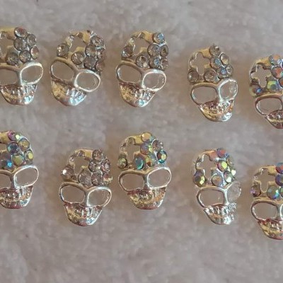 Dez botões prateados em forma de caveira com pedras brilhantes em tecido branco