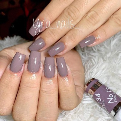 Unhas compridas quadradas com verniz cinza e garrafa de verniz ao lado