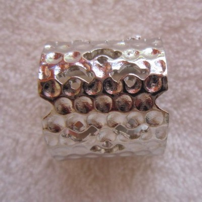 Anel largo prateado texturizado sobre pano bege