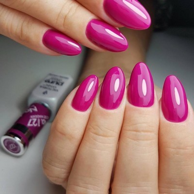 Mãos com unhas rosa vivo brilhantes e tubos de verniz gel ao fundo