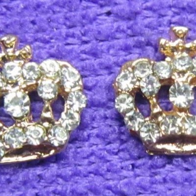 Brincos de coroa dourados com pedras brilhantes sobre fundo roxo texturizado