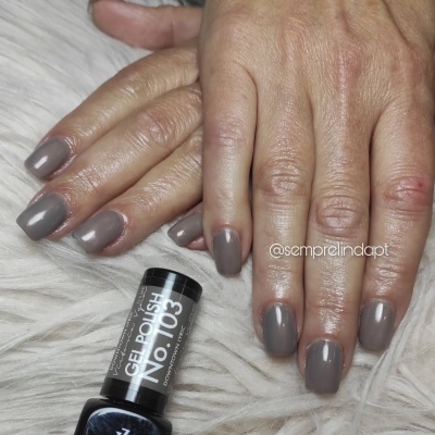 Mãos com unhas pintadas de verniz gel cinza com frasco de verniz gel preto