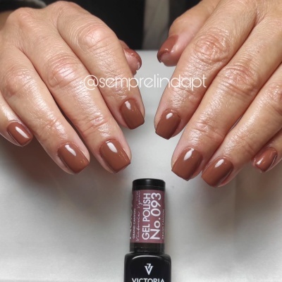 Mãos com unhas pintadas de verniz gel castanho claro e frasco de verniz gel Victoria Vynn No. 093