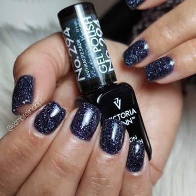 Unhas curtas pintadas com esmalte glitter escuro brilhante segurando frasco de esmalte Victoria Vynn