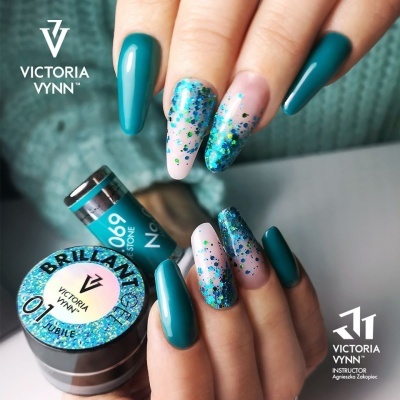 Mãos com unhas decoradas em verniz verde azulado e glitter, com frascos de gel para unhas Victoria Vynn.