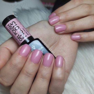 Mãos femininas com verniz de gel rosa e frasco de verniz GEL POLISH Nº 015