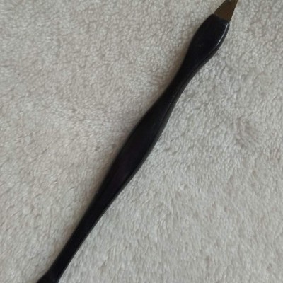 Ferramenta preta alongada com ponta metálica bifurcada numa superfície branca texturada.